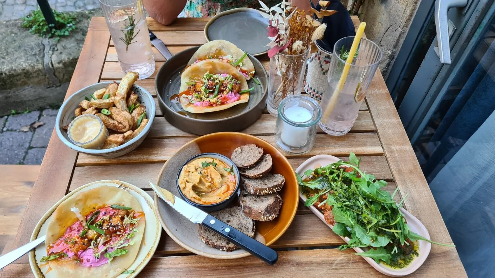 Table dressée en terrasse : tapas, houmous, frites maison et boissons fraîches
