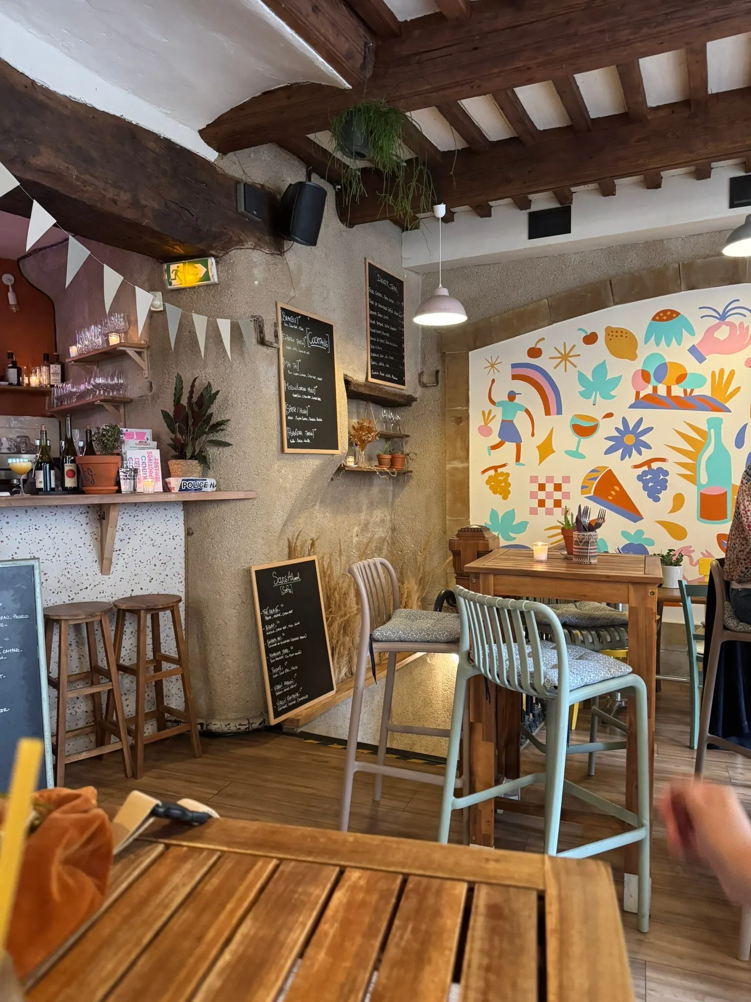 Salle de La Station : poutres apparentes, fresque colorée, tabourets hauts et petites ardoises